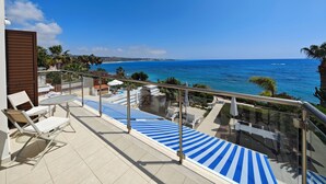 Uma varanda com vista para o mar, cadeiras de descanso e guarda-corpo de vidro.