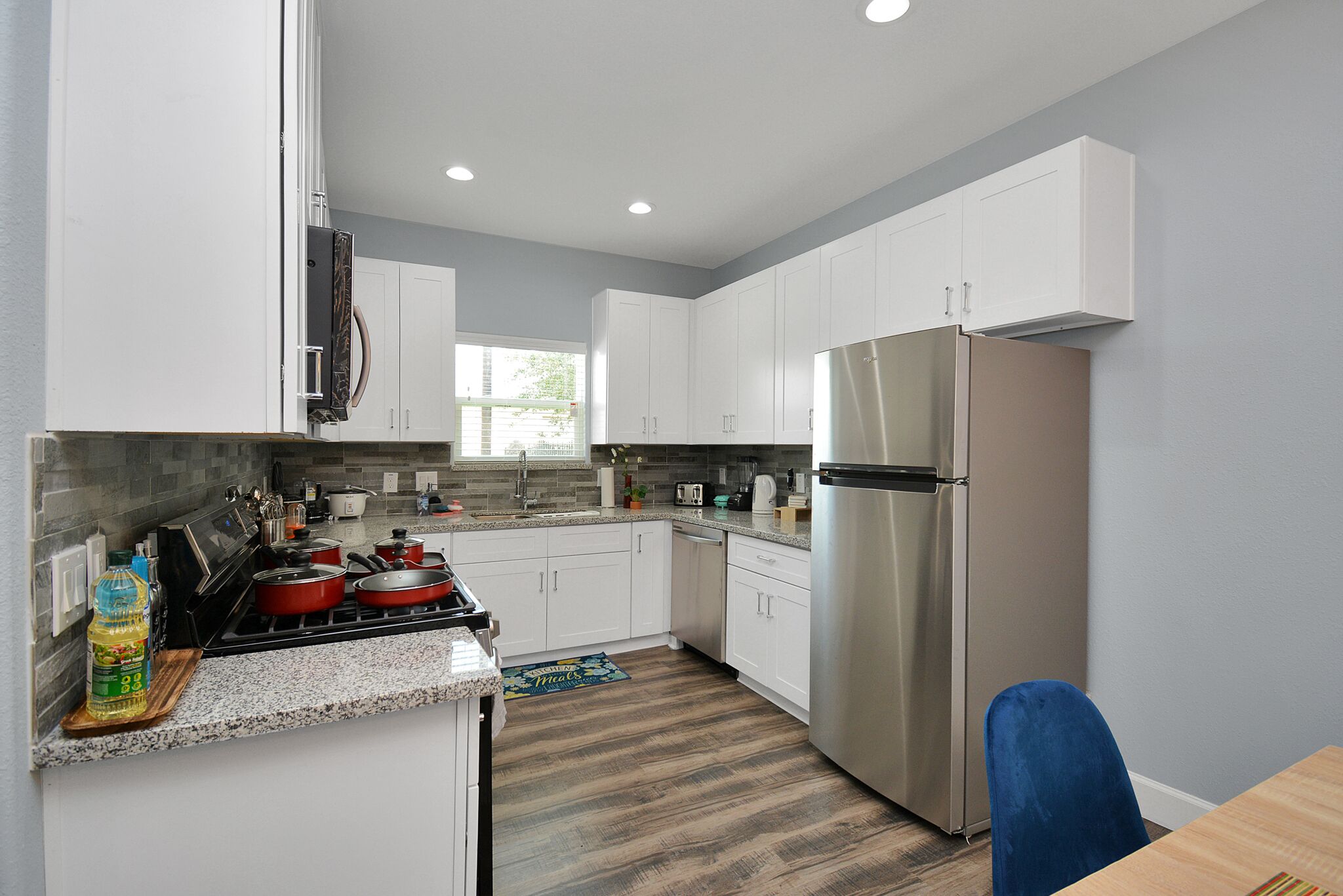 A modern kitchen with white cabinets, stainless steel appliances, and a wooden floor.