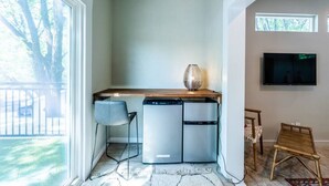 A compact kitchen with a built-in dishwasher, a dining area with a chair, and a large window offering a view of trees. - Cozy Boho Guesthouse + Rooftop Deck in the Trees (Austin)