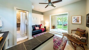 A modern living room with a sofa, a coffee table, and a chair. There is a ceiling fan, a window, and a door leading to another room. - Cozy Boho Guesthouse + Rooftop Deck in the Trees (Austin)