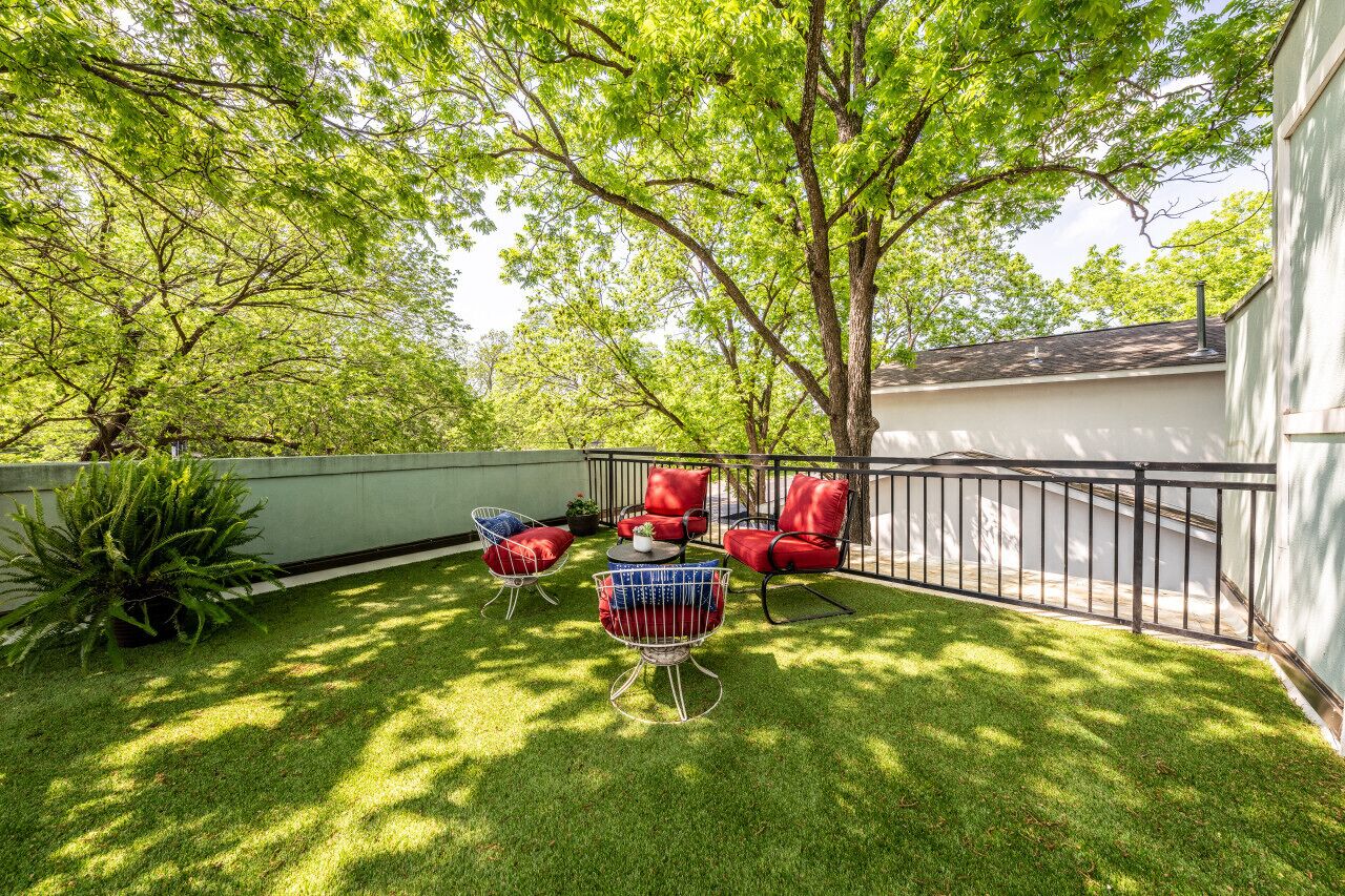 A backyard with a lawn, a tree, and outdoor furniture including red chairs and a table.