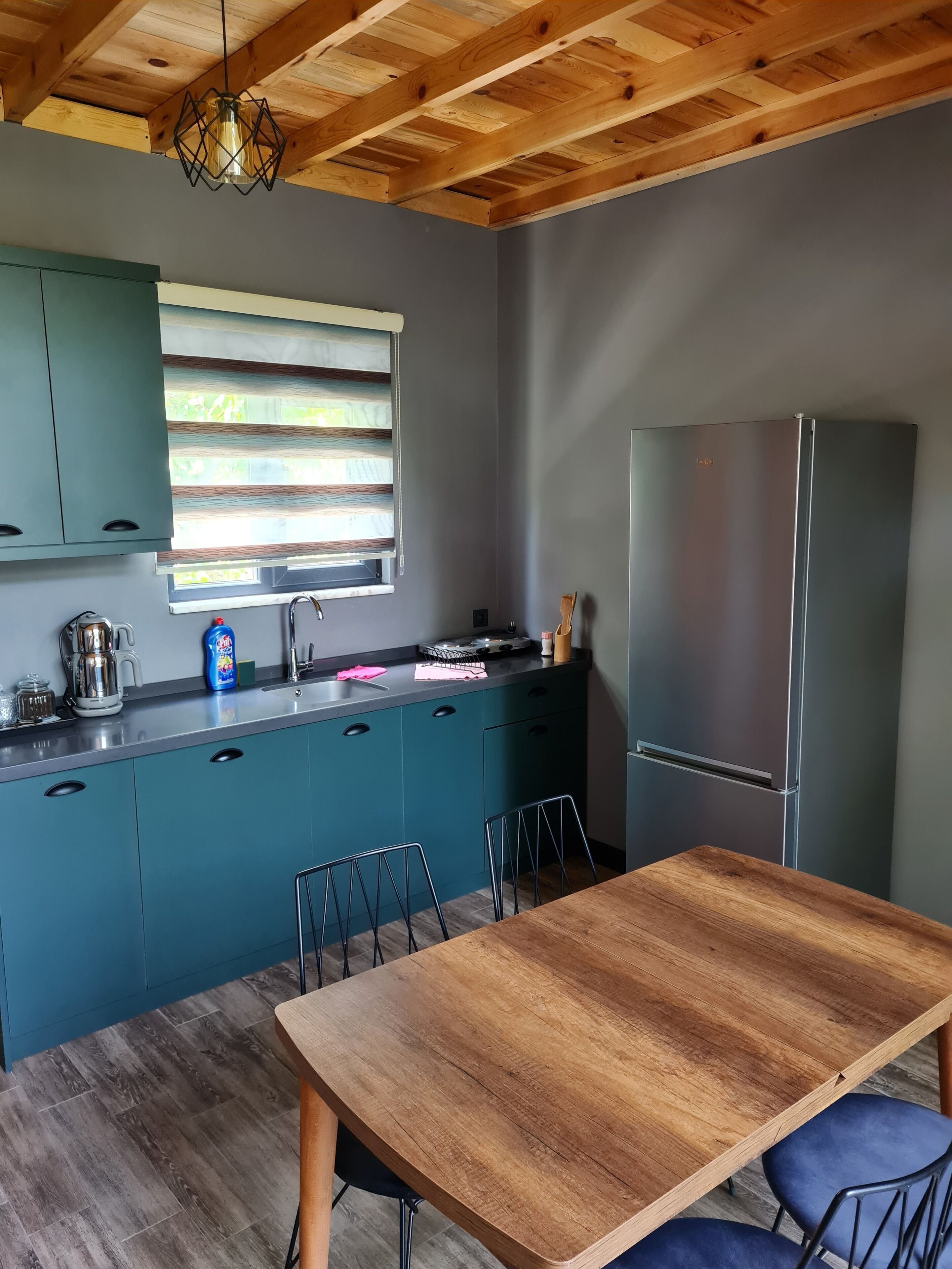 Una cocina moderna con armarios azul turquesa, una mesa de comedor de madera y un refrigerador de acero inoxidable.