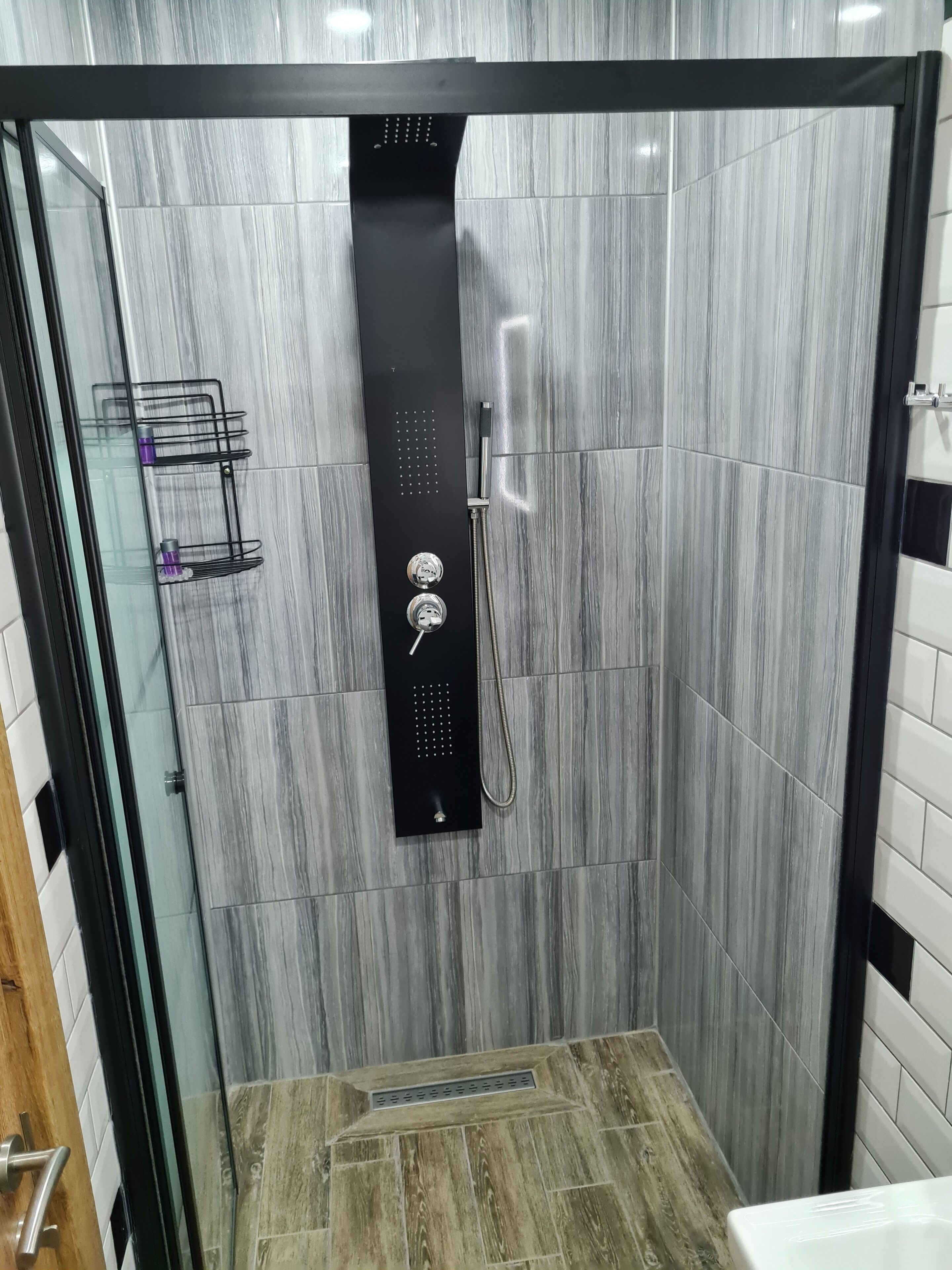 A modern shower enclosure with a glass door, a black control panel, and a showerhead.
