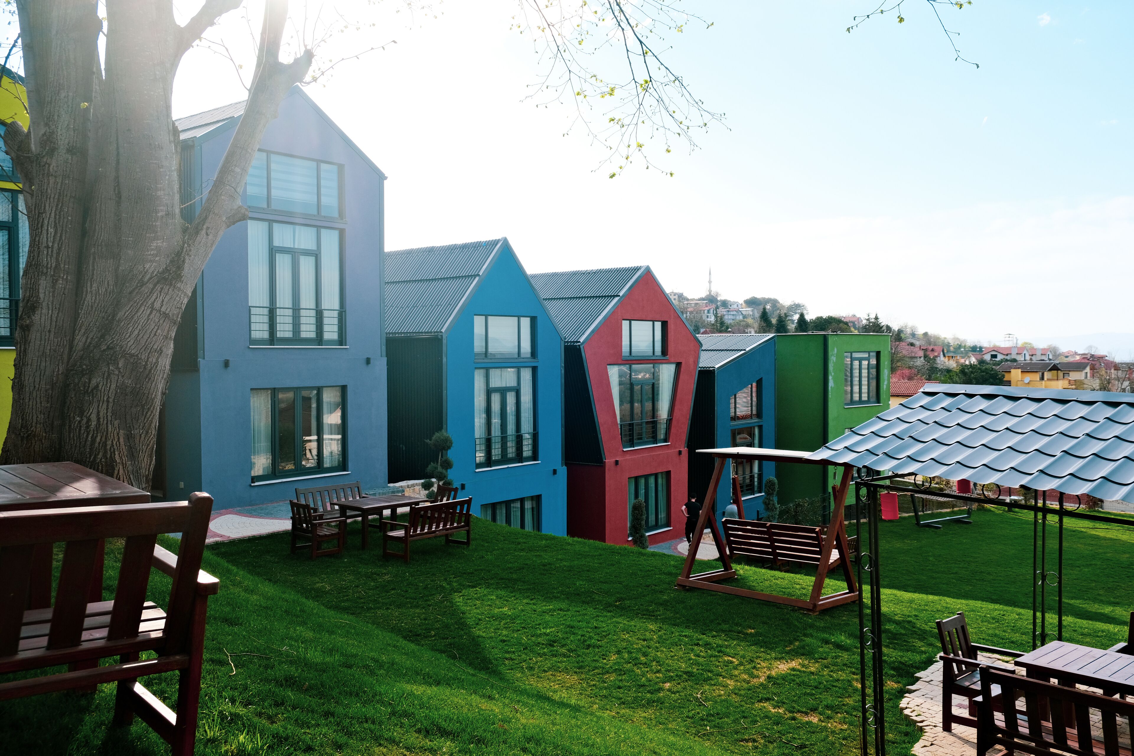 Un edificio moderno con fachada azul, roja y verde, un césped cuidado y mobiliario exterior.