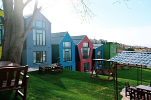 Un edificio moderno con fachada azul, roja y verde, un césped cuidado y mobiliario exterior.
