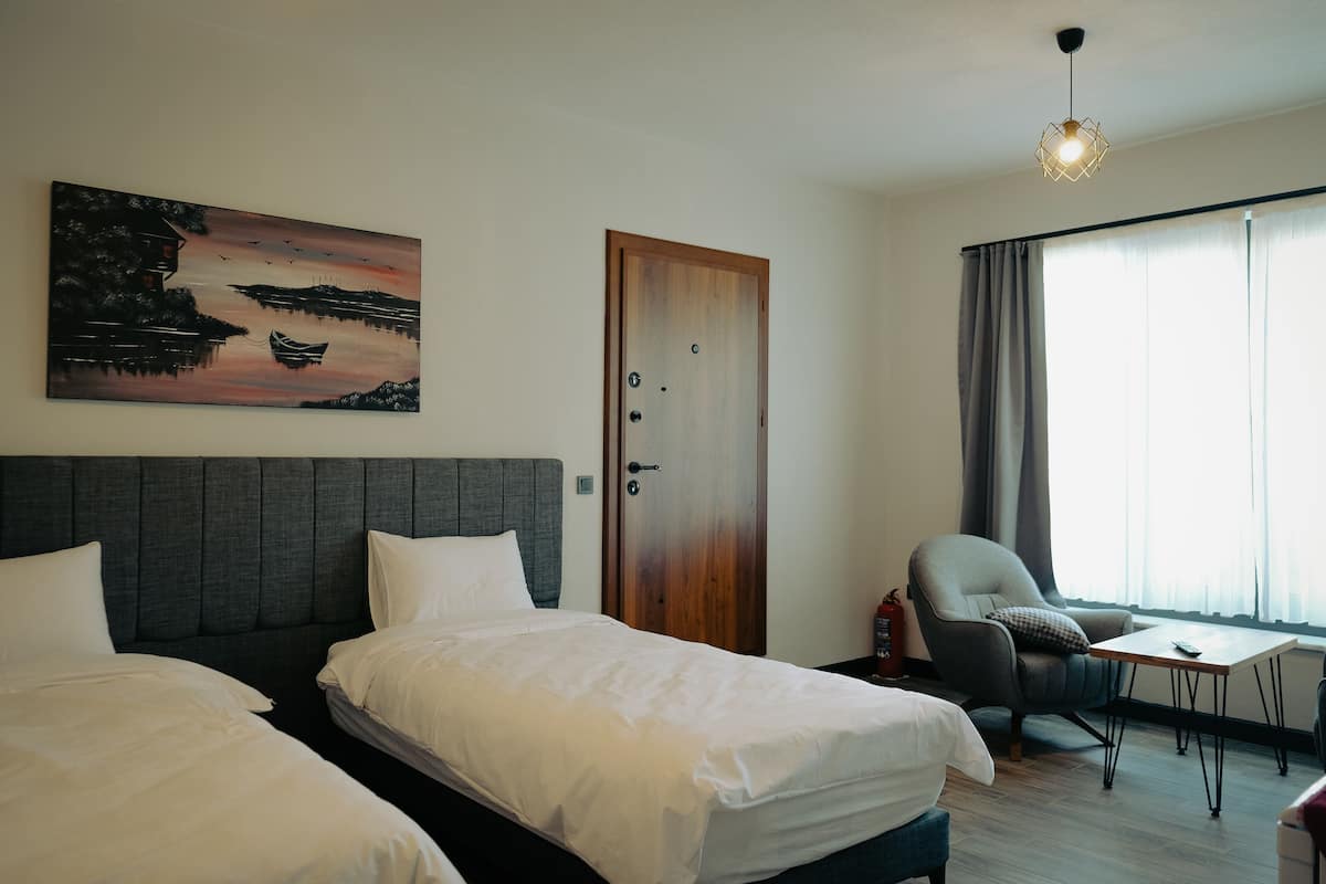 Ett hotellrum med två sängar, ett skrivbord, en stol, en tavla och en dörr.