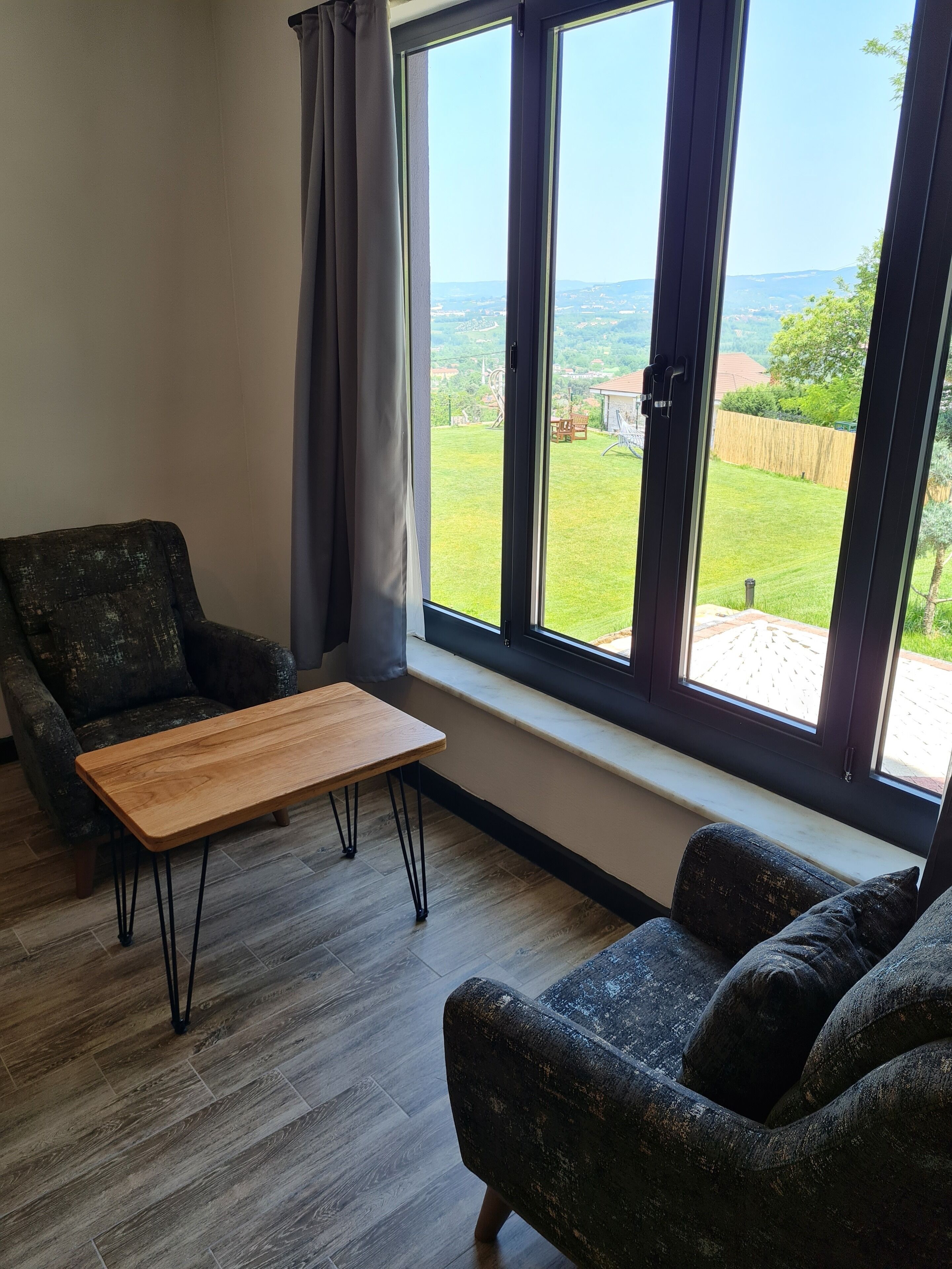 A room with a large window, a wooden table, a dark armchair, and a sofa.
