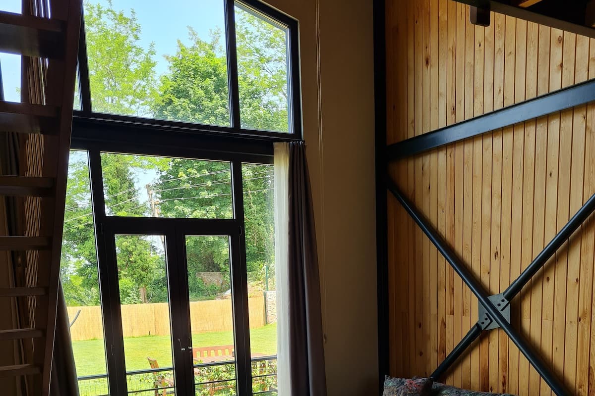 Ett rum med ett stort fönster, ett trägolv, en soffa, ett bord och en stol.