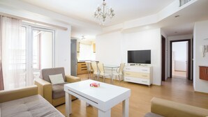 A modern living room with a sofa, armchairs, a TV, a dining table, and a chandelier.