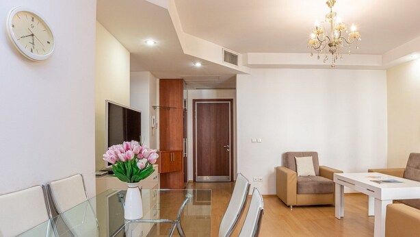 A modern living room with a glass dining table, beige sofa, and a chandelier.