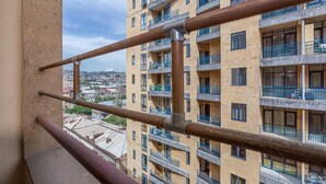 A multi-story residential building with balconies, a view of the cityscape, and a metal railing in the foreground.