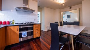 A modern kitchen with a gas stove, oven, and stainless steel range hood. There is a dining area with a white table and black chairs. - Wiltshire | Large & Spacious (Melbourne)