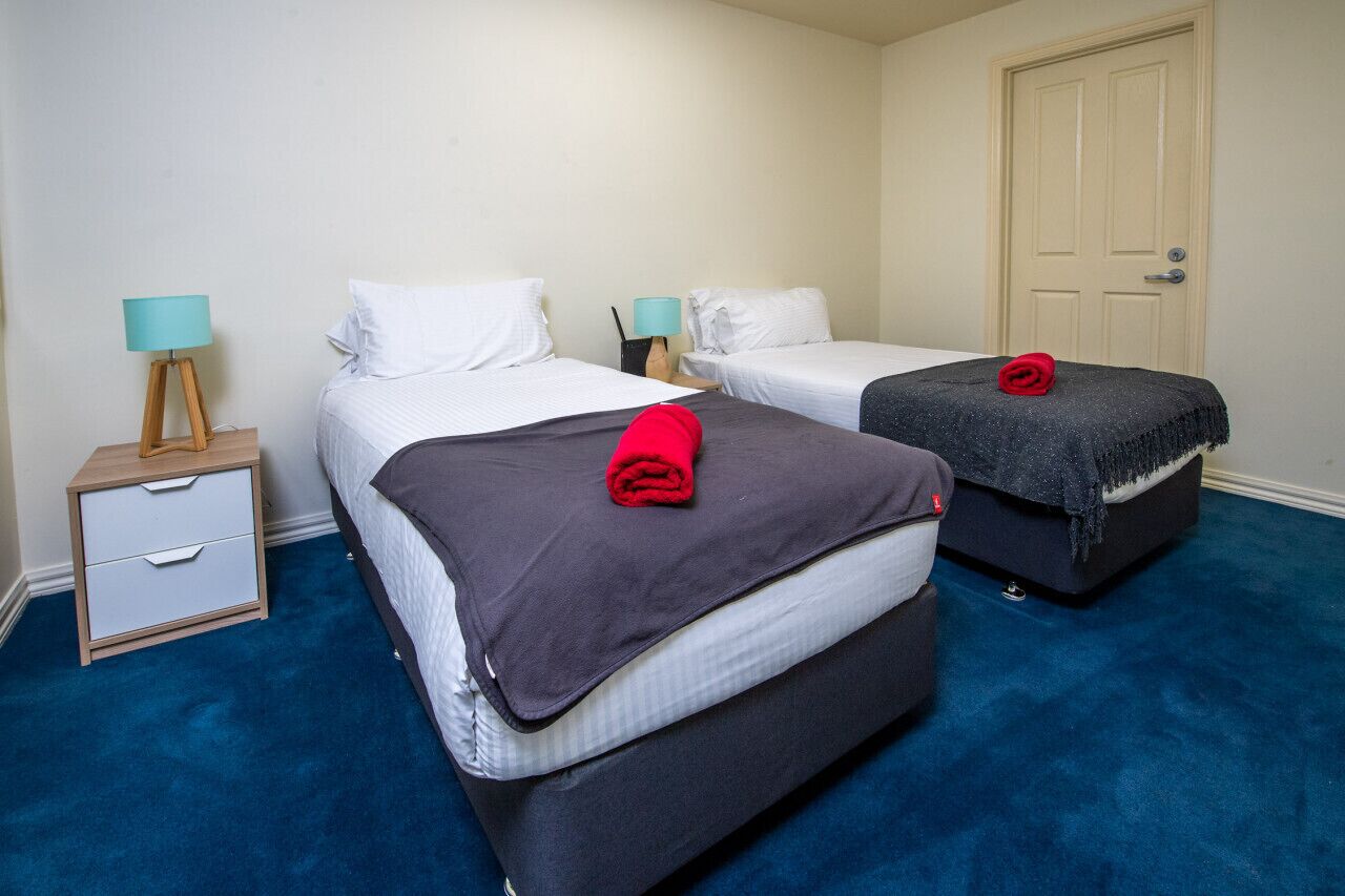 Habitación de hotel con dos camas, una mesita de noche y una puerta.