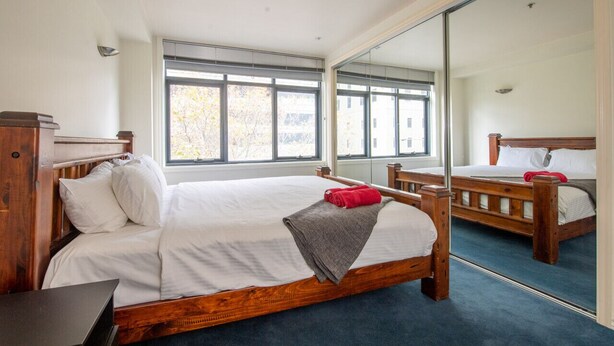 A bedroom with a wooden bed, a desk, and a large mirror. - Wiltshire | Large & Spacious (Melbourne)