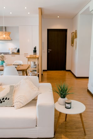A modern living room with a white sofa, a small round table with a plant, and a wooden floor.
