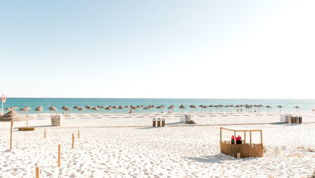 Een strand met rijen rieten parasols en een houten constructie.