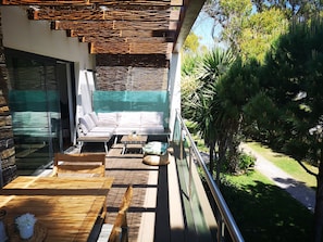 Enjoy the serene views of the surrounding greenery from this outdoor balcony with a seating area and metal railing.