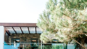 Een modern gebouw met een gevel van natuursteen, een balkon met glazen hekwerk en een grote dennenboom voor op de foto.