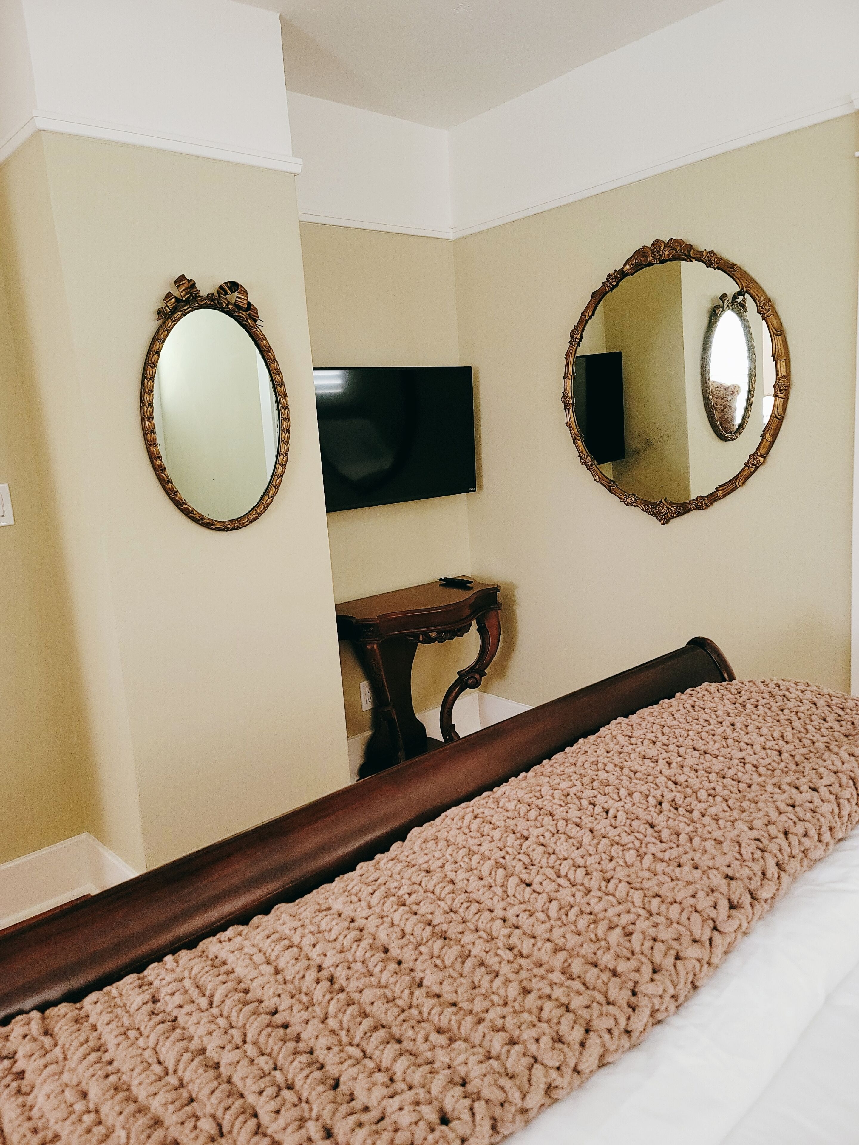 A bedroom with a bed, two wall-mounted mirrors, a television, and a small wooden table.