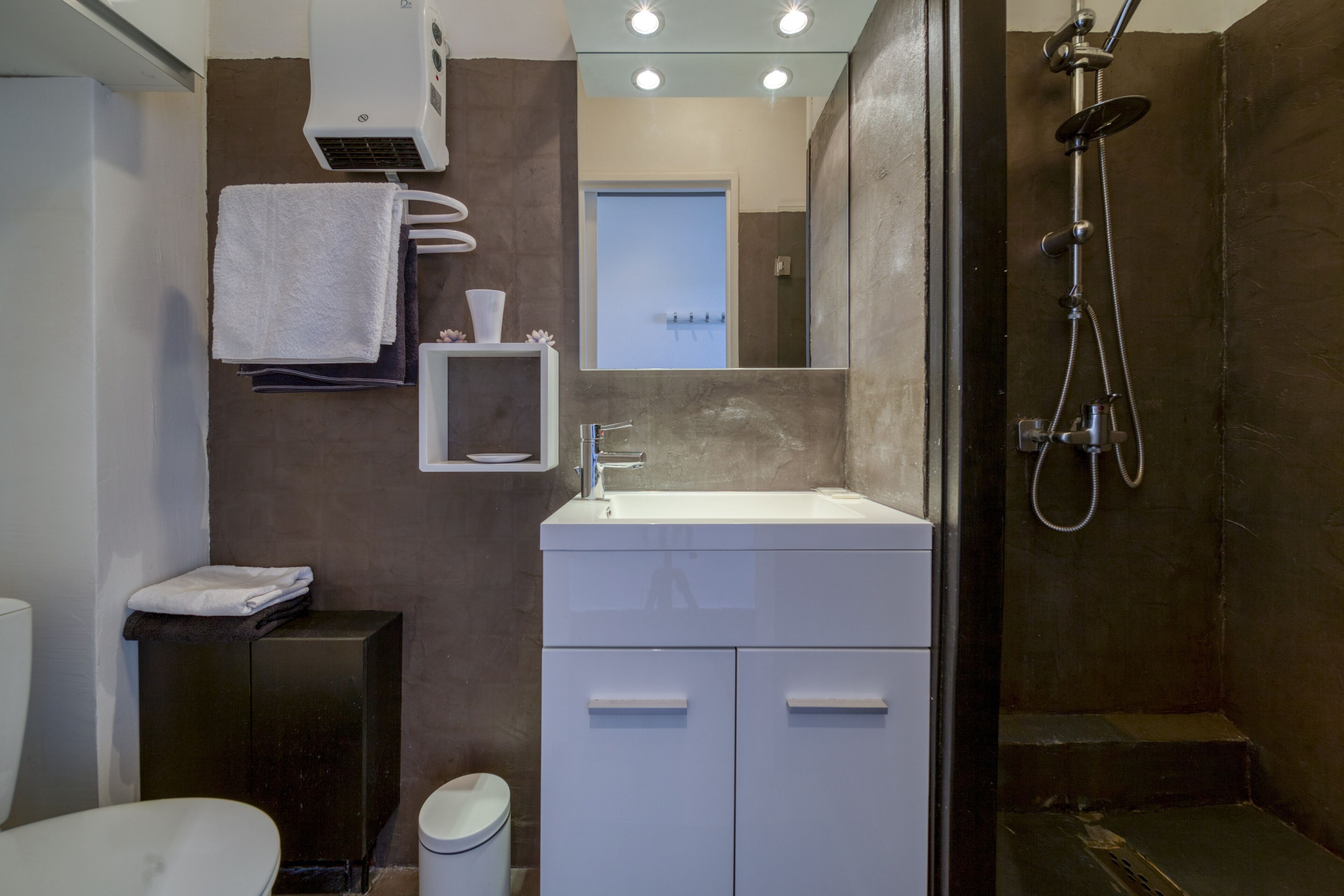 Un baño moderno con un lavamanos blanco, un espejo, un perchero para toallas y una ducha.