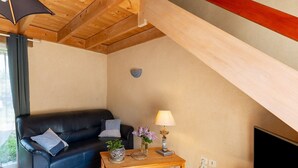 A cozy living room with a black leather sofa, a wooden coffee table with decorative items, a lamp, and a television. - Ty ar Hezeg - Gîte 3e avec terrasse privative (Telgruc-sur-Mer)