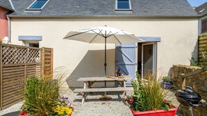 A patio with a table, umbrella, and barbecue grill. - Ty ar Hezeg - Gîte 3e avec terrasse privative (Telgruc-sur-Mer)