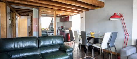 Een moderne woonkamer met een zwarte leren bank, een eethoek met stoelen en een tafel, en een rode vloerlamp.