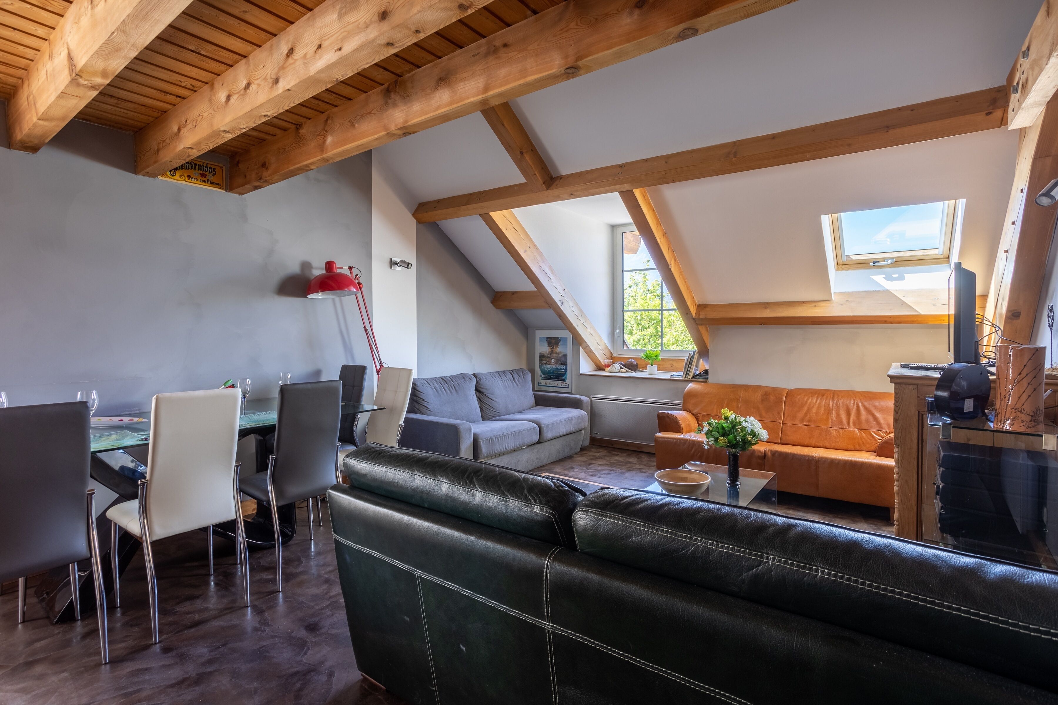 Un saló d'estil loft amb un sostre alt, bigues de fusta, zona de dinar amb taula i caires, un sofà i una finestra amb vistes.