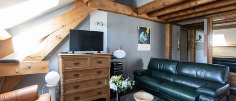 A modern living room with a wooden ceiling, a black leather sofa, a wooden cabinet, and a glass coffee table.
