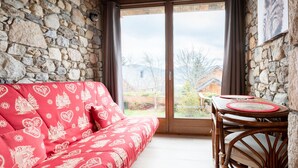 Ein Raum mit Steinwänden, einem rot gemusterten Sofa und einem Holztisch mit Stühlen.