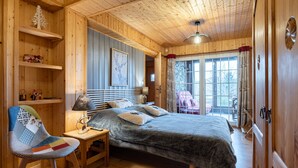 Ein gemütlicher Holzraum mit einem Bett, einem Sessel, einem Tisch und einem Fenster mit Vorhängen.