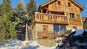 Eine Holzhütte mit Steinunterbau, einem Balkon und einer Treppe, die zum Eingang führt.