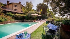 A swimming pool with lounge chairs and umbrellas, surrounded by greenery and a stone building. - Villa with panoramic pool • Passignano sul Trasimeno, Umbria (Passignano sul Trasimeno)