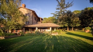 A stone house with a tiled roof, surrounded by a well-maintained lawn and trees. - Villa with panoramic pool • Passignano sul Trasimeno, Umbria (Passignano sul Trasimeno)