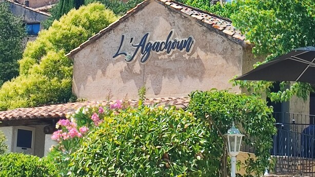 A building with a sign reading "L'Agachorn" surrounded by greenery and other buildings. - Vilajoun (Joucas)