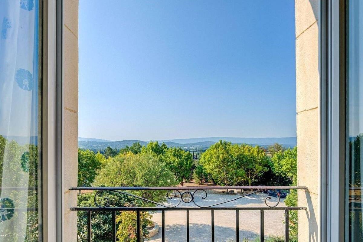Un balcón con barandilla de metal que ofrece vistas a un paisaje con árboles y colinas a lo lejos.