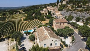 A rural village with terraced vineyards, a stone building with a pool, and a hilltop structure. - Vilajoun (Joucas)