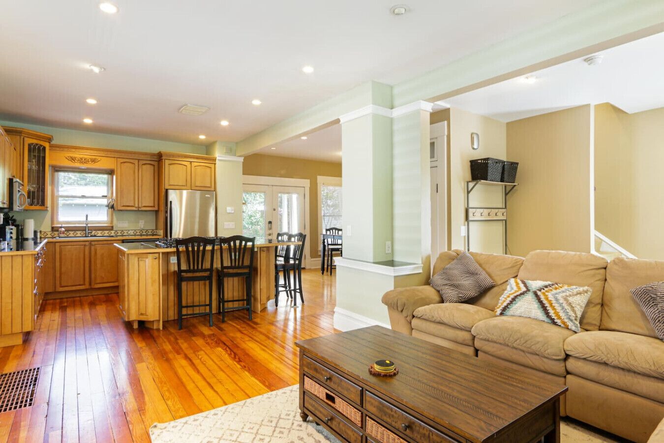 A spacious living area with a sofa and a coffee table, a kitchen with wooden cabinets and a central island, and a dining area with chairs.