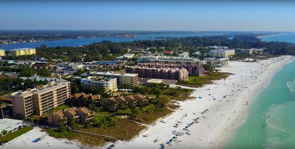 A coastal resort with beachfront properties, a sandy beach, and a view of the ocean and distant cityscape. - Midnight Cove #532, Bayside in Siesta Key, FL, 2BR-1 1/2 BA, 3rd Floor Walk-Up (Sarasota)