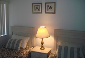 A neatly made bed with striped pillows, a bedside lamp, and two framed pictures on the wall. - Midnight Cove #532, Bayside in Siesta Key, FL, 2BR-1 1/2 BA, 3rd Floor Walk-Up (Sarasota)