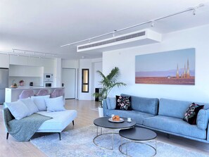 A modern living room with a sofa, coffee table, and a painting on the wall. - Seafront penthouse - terrace, AC, lift & parking (Tel Aviv-Yafo)