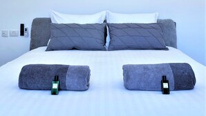 A bed with grey bedding, two pillows, and two rolled towels. - Seafront penthouse - terrace, AC, lift & parking (Tel Aviv-Yafo)