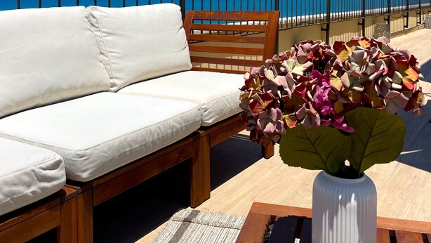 A balcony with a white cushioned sofa, a wooden bench, and a vase with flowers. - Seafront penthouse - terrace, AC, lift & parking (Tel Aviv-Yafo)