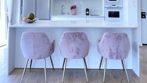 A modern kitchen with white cabinetry, a central island, and three pink chairs. - Seafront penthouse - terrace, AC, lift & parking (Tel Aviv-Yafo)