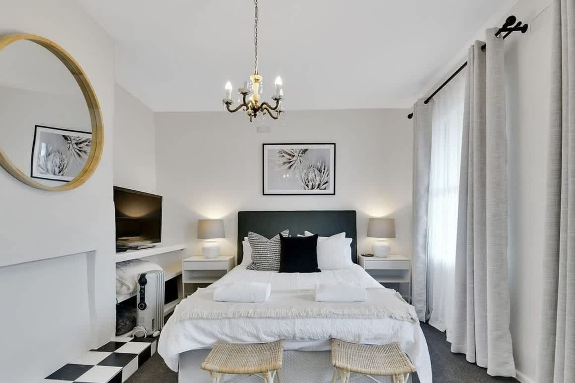 A hotel room with a large bed, bedside tables, a chandelier, a mirror, and artwork on the walls.