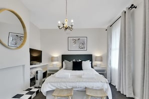 A hotel room with a large bed, bedside tables, a chandelier, a mirror, and artwork on the walls.