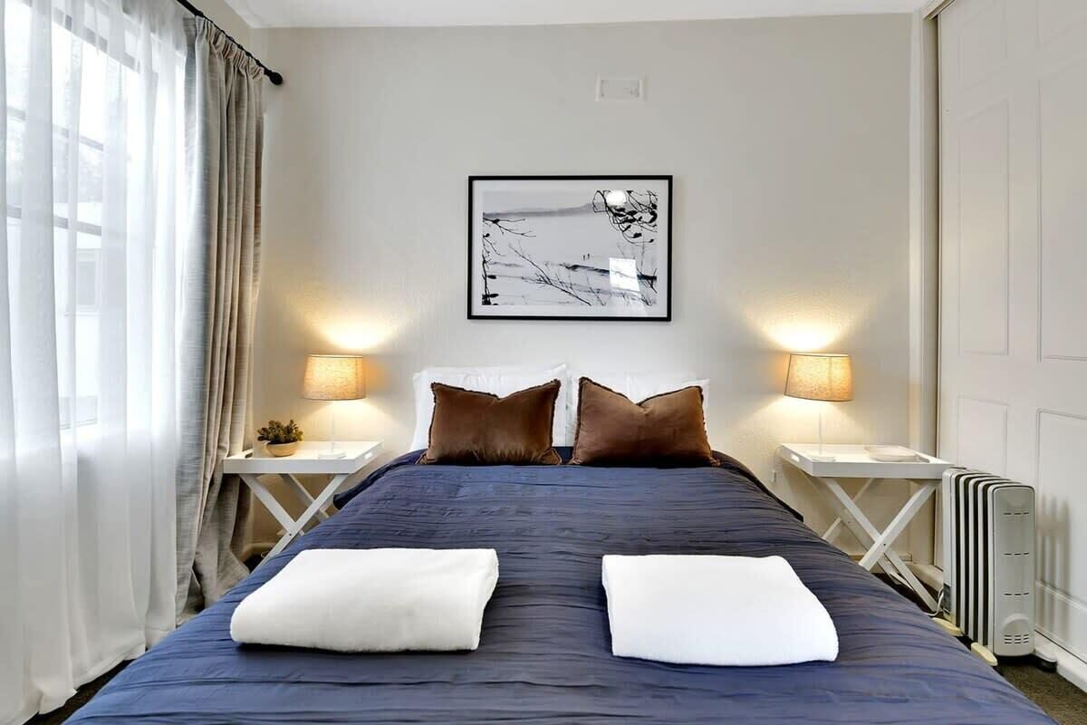 A hotel room with a large bed, two bedside lamps, a radiator, and a framed abstract painting on the wall.