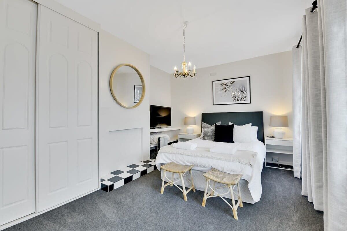 A bedroom with a bed, two nightstands, a round mirror, a chandelier, and a checkered floor pattern.