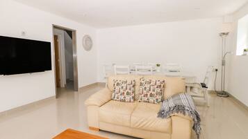 A modern living room with a sofa, a coffee table, a TV, and a dining area with chairs and a table.