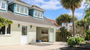 A two-story house with a covered patio, a small boat model in the window, and a palm tree in the yard. - Wheatlands (Hayling Island)
